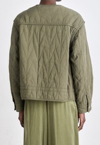 Kurtka w oliwkowym kolorze z pikowanym wzorem, charakteryzująca się luźnym krojem, opadającymi ramionami oraz metalowymi zapięciami na zatrzaski, wykonana z teksturowanej tkaniny w diamentowy wzór.