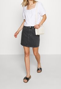 Vit blus med puffärmar och knapprad, kombinerad med en svart denimkjol och svarta halksandaler. Tillbehören inkluderar en liten vävd väska.