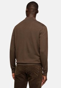 Brown knitted sweater with a ribbed collar, long sleeves, and a textured fabric. Worn over dark brown corduroy pants. Back view.