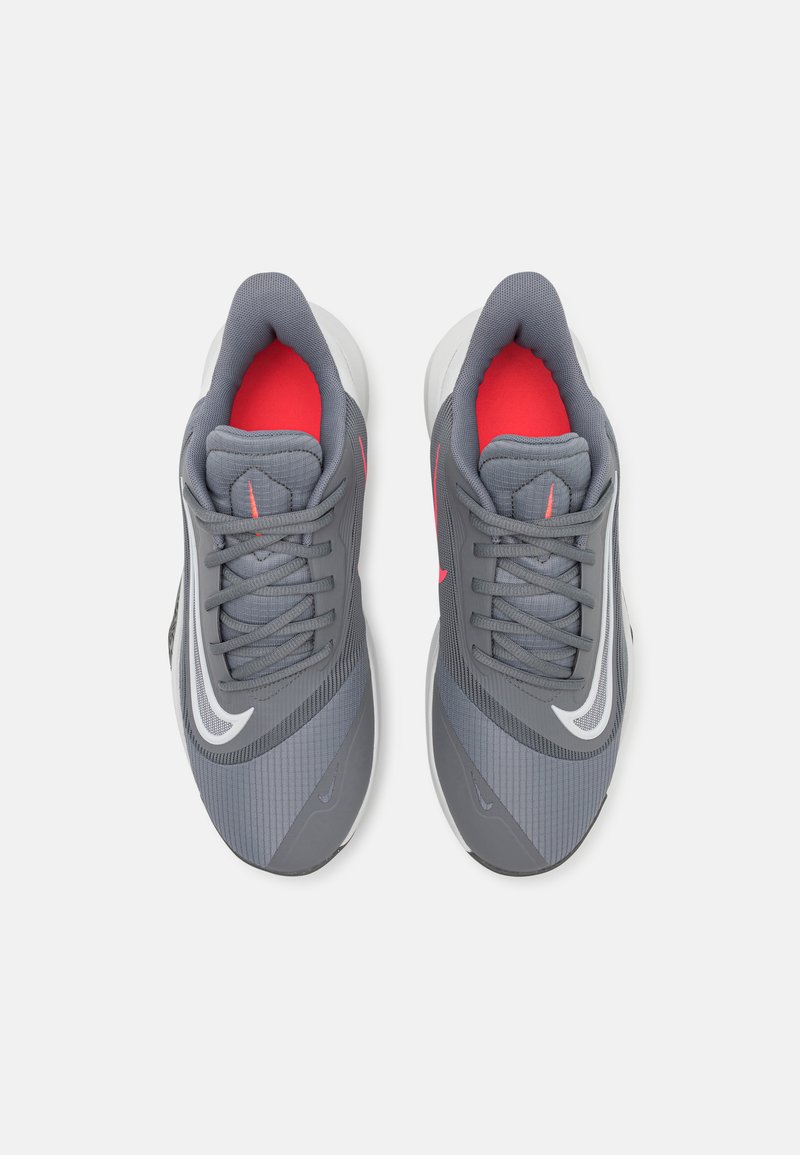 Chaussures de sport gris avec une tige texturée, accents rouges à l'intérieur, logo swoosh blanc et design épuré. Nouées avec des lacets gris.