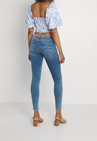 Top corto azul con estampado floral y mangas abullonadas, combinado con unos jeans oscuros ajustados de cintura alta y sandalias de tacón bloque en color tostado.