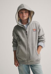 Grauer Kapuzenpullover mit Reißverschluss, weichem Innenfutter, Kordelzug an der Kapuze und Fronttaschen. Verfügt über ein gestreiftes Innenfutter und ein Logo-Patch auf der Brust.