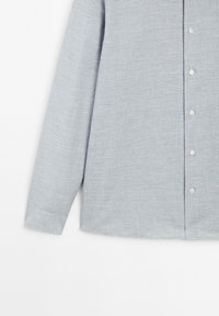 Lichtgrijze langekleurige blouse gemaakt van gestructureerde stof, met een knoopsluiting aan de voorkant met witte knopen en een rechte zoom.