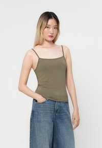 Top verde aceituna, camiseta ajustada con tirantes finos, textura suave. Combinada con jeans de mezclilla azul de tiro alto y corte holgado.