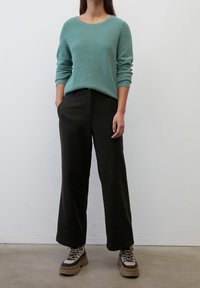 Lys blå struktureret strik sweater, høj talje sorte vide bukser og kraftige beige og sorte snørebåndsstøvler. Glatte, bløde stoffer.
