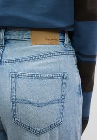 Ανοιχτό μπλε τζιν παντελόνι με λεπτομέρειες στην πίσω τσέπη και ταμπέλα από ταμπά δέρμα με την επιγραφή "Pepe Jeans London" στη μέση.