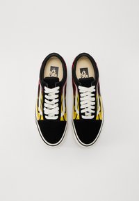 Zapatillas de ante negras y amarillas con diseño de llamas, cordones blancos y puntera negra en contraste. El interior presenta el logo de la marca en la plantilla.