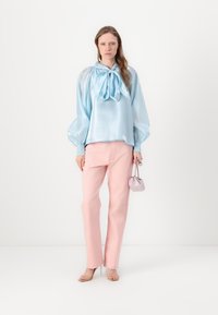 Camicia di raso azzurro chiaro con un fiocco al colletto, abbinata a pantaloni dritti rosa chiaro e una borsa piccola lilla.
