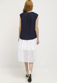 Námořnicky modrý top s krátkým rukávem a záhybem na zádech, kombinovaný s bílou sukní s otevřenými očkovými vzory, doplněný béžovými lodičkami na vysokém podpatku.