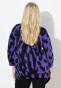 Fioletowo-czarny sweter z odważnym wzorem w prążki tygrysa, o luźnym kroju i rękawach o długości do łokcia. Dzianina o fakturowanej strukturze.