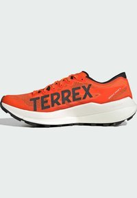 Lyse orange trail løbesko med sort sål, stor "TERREX"-tekst, snøresystem og hvid polstret mellemsål mærket "Lightstrike."