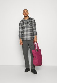 Pilkas plaid flanelinis marškinis ilgomis rankovėmis, pilkos kelnės ir rožinė rankinė su dviem rankenomis bei užtrauktuko kišene. Juodi batai.