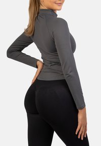 Sivý priliehavý top s dlhým rukávom a vysokým golierom, s kontrastným šitím, skombinovaný s čiernymi legínami s vysokým pásom, ktoré zvýrazňujú kontúry tela.