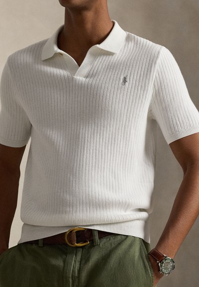 White ribbed short-sleeve polo shirt with a V-neck collar and subtle logo. Worn with green pants, featuring a brown belt and watch.