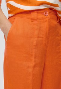 Oranžid linased püksid siledate tekstuuriga, külgpocketiga ja roosa nööbiga vööl.