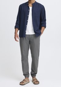 Marineblå linned skjorte med opredte ærmer, hvid crew neck t-shirt, grå bukser med elastik i manchetten og brune sandaler med remme.