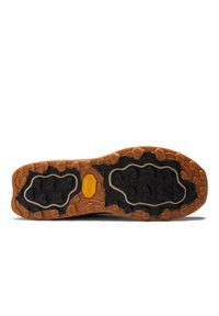 Traction outsole of a shoe featuring a mix of black rubber and tan accents, with a textured surface and a prominent logo at the center.