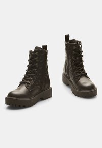 Botas de tobillo de cuero negro con un patrón acolchado, parte delantera con cordones, cremallera lateral, suela gruesa y un lazo en la parte posterior para facilitar su puesta.