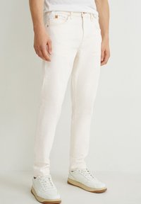 Jeans de mezclilla blanca con un ajuste slim, con un diseño clásico de cinco bolsillos y costuras sutiles. Combinados con zapatillas blancas y una camisa ligera.