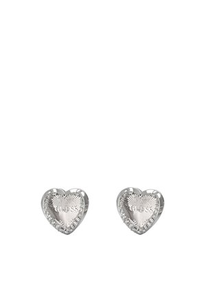 Orecchini a perno a forma di cuore in metallo argentato, caratterizzati da una texture rigata e accenti scintillanti lungo il bordo. Incisione "GUESS" sulla superficie.