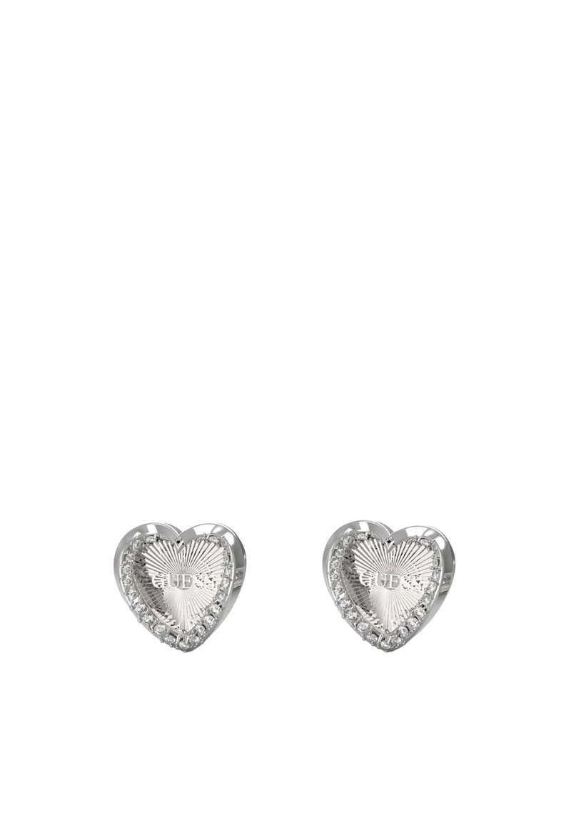 Orecchini a perno a forma di cuore in metallo argentato, caratterizzati da una texture rigata e accenti scintillanti lungo il bordo. Incisione "GUESS" sulla superficie.