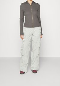 Haut à fermeture éclair gris avec capuche et manches longues, associé à un pantalon cargo gris clair comprenant plusieurs poches et une coupe décontractée.