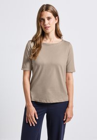 Beige krátký rukáv top s kulatým výstřihem, měkkou texturou a uvolněným střihem, v kombinaci s tmavě modrými kalhotami. Jednoduchý design, bez vzorů nebo akcentů.