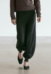 Schwarze, weiche Stoffjogginghosen mit lockerem Schnitt, nach unten zulaufenden Bündchen und elastischem Bund, kombiniert mit schlichten schwarzen Ballerinas.