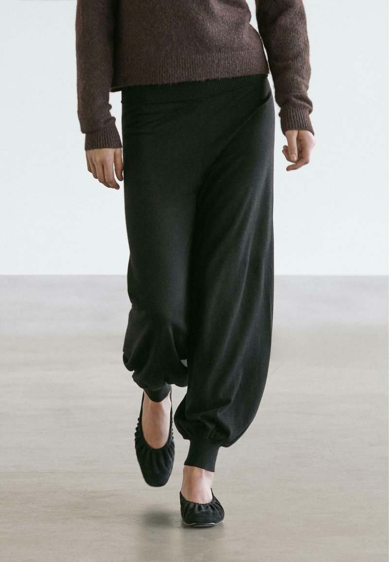 Sorte joggingbukser i blødt stof med løs pasform, tilspidsede manchetter og elastisk talje, kombineret med enkle sorte ballerinaer.