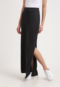 Zwarte maxi rok van zachte stof, met een hoge split aan één kant. Gecombineerd met een wit t-shirt en witte sneakers voor contrast.