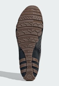 Μαύρη σόλα αθλητικού παπουτσιού με υφή από καφέ καουτσούκ. Διαθέτει μοτίβο πρόσφυσης πολλαπλών κατευθύνσεων και λεπτομέρειες με λογότυπο στα πλάγια.