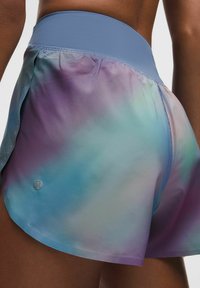 Tie-dye löparshorts med en ljusblå midja. Tyget har en gradient av lila, blått och teal, med subtila prickmönster.