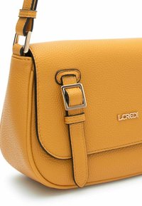 Bolso cruzado de piel texturizada amarilla, con cierre de solapa, correa ajustable y detalles en metal plateado. Logo de la marca visible.