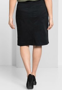 Falda lápiz de mezclilla negra con corte recto, dos bolsillos traseros y detalles de costura. Llevada con zapatos de tacón altos negros.