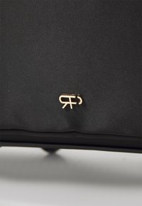 Fekete nylon táska arany fém logóval, sima textúrával és minimalista dizájnnal. A felülete enyhén textúrált.