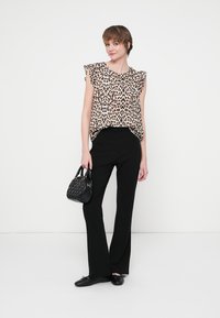 Blusa de estampado de leopardo con mangas acampanadas, combinada con pantalones de campana negros. Los accesorios incluyen un pequeño bolso negro.