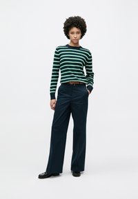 Πλεκτό πουλόβερ με λωρίδες σε πράσινο και λευκό χρώμα, με στρογγυλή λαιμόκοψη, συνδυασμένο με παντελόνια φαρδιάς γραμμής σε ναυτικό μπλε με ψηλή μέση και μαύρα παπούτσια.