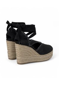 Espadrillas nere con zeppa in juta intrecciata, con punta aperta e cinturini incrociati in tessuto. Parte superiore testurizzata con dettagli decorativi vicino alla caviglia.