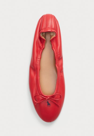 Punane naha ballet-sandaal elastse avausega, beež vooder, ja väike tumesinine logo, mis on tikitud paela detaili lähedale.