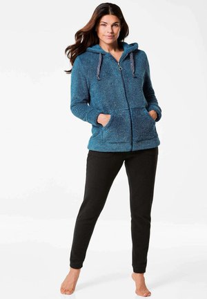 Blauer strukturierter Zip-Hoodie mit Kapuze, Schnürzügen und Fronttaschen, kombiniert mit enganliegenden schwarzen Hosen.