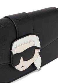 Czarna skórzana kopertówka o teksturowanym wykończeniu, z białą i czarną aplikacją przedstawiającą postać w okularach przeciwsłonecznych z przodu. Zapięcie magnetyczne.