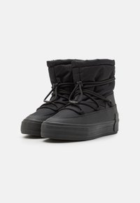 Botas altas negras de cuero sintético con exterior de nylon acolchado, puntera redondeada, suela de goma gruesa y cordones ajustables. Los detalles texturizados añaden interés visual.