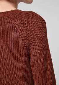 Gebreide trui in een roestkleur, met een gestructureerd patroon, ronde halslijn en geribbelde manchetten. Detail benadrukt het geweven ontwerp.