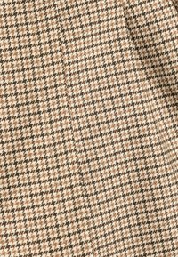 Bruin en crèmekleurig houndstooth patroon geweven stof met een textuur, met kleine geometrische vormen in een geweven ontwerp.