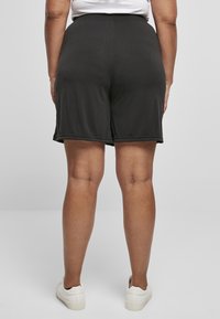 Sorte shorts laget av lett stoff med elastisk midjebånd. Har en rett skåret og ferdige kanter, brukt med hvite joggesko.
