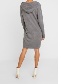 Grijze gebreide jurk met een capuchon, lange mouwen en een losse pasvorm, die net boven de knieën eindigt. Gecombineerd met crèmekleurige enkellaarsjes.