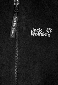 Czarna polarowa kurtka z pełnym zamkiem. Posiada logo "Jack Wolfskin" w białym haftowanym na piersi oraz przy zamku. Miękka tekstura.