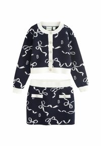 Set di maglina blu navy composto da due pezzi con motivi a fiocco bianchi. Il cardigan presenta un colletto rotondo e bottoni; la gonna ha una vita alta e tasche decorative.