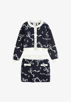 Navy blue dzianinowy dwu-elementowy zestaw z białymi wzorami w kokardy. Kardigan ma okrągły dekolt i guziki; spódnica ma pasek w talii i dekoracyjne kieszenie.