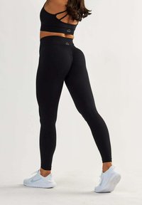 Leggings noirs taille haute en tissu extensible, au design sans coutures et à la texture douce, associés à des baskets de sport blanches.